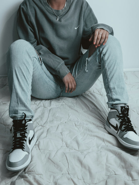 man in gray sweater and gray denim jeans sitting on bed