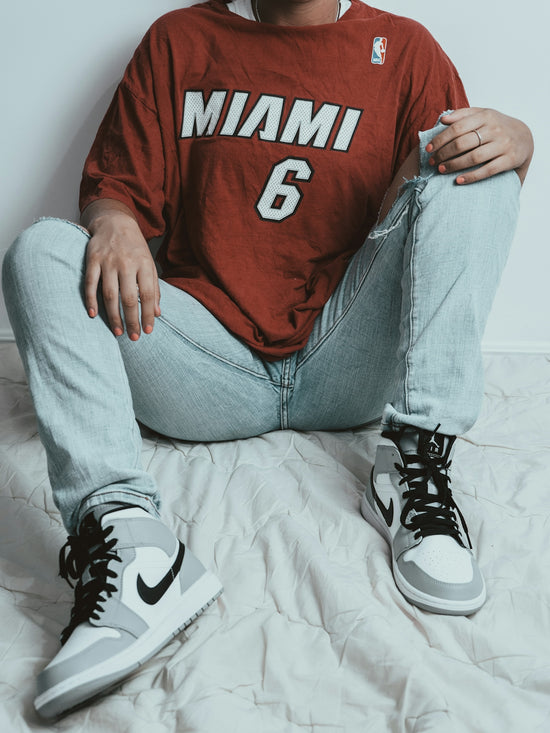 person in red and white hoodie and gray denim jeans sitting on white bed
