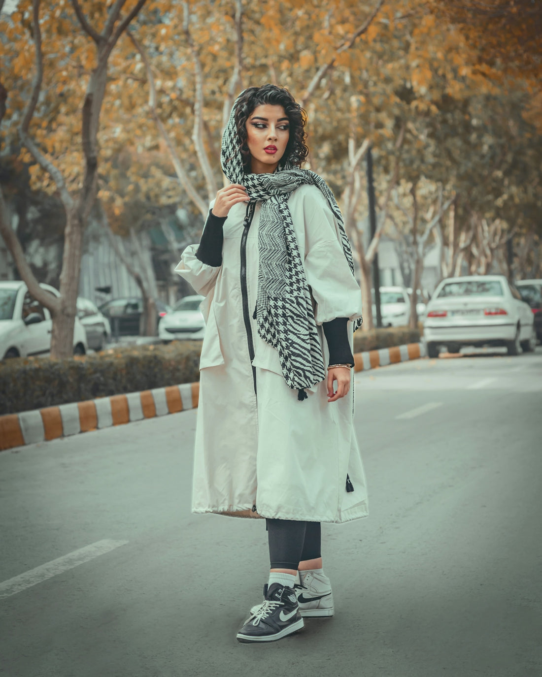 a person in a long coat and scarf standing in a parking lot