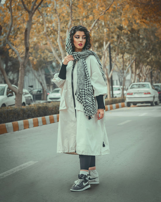 a person in a long coat and scarf standing in a parking lot