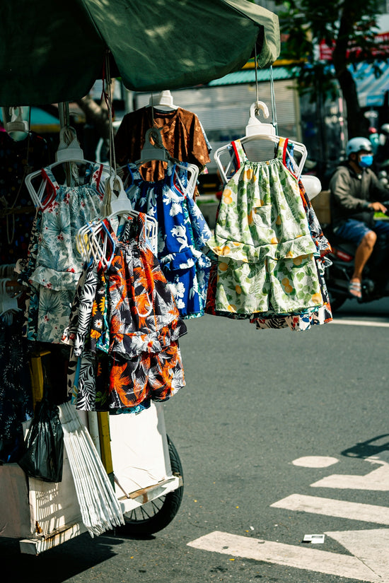 Colorful children's dresses displayed on a street vendor's cart.