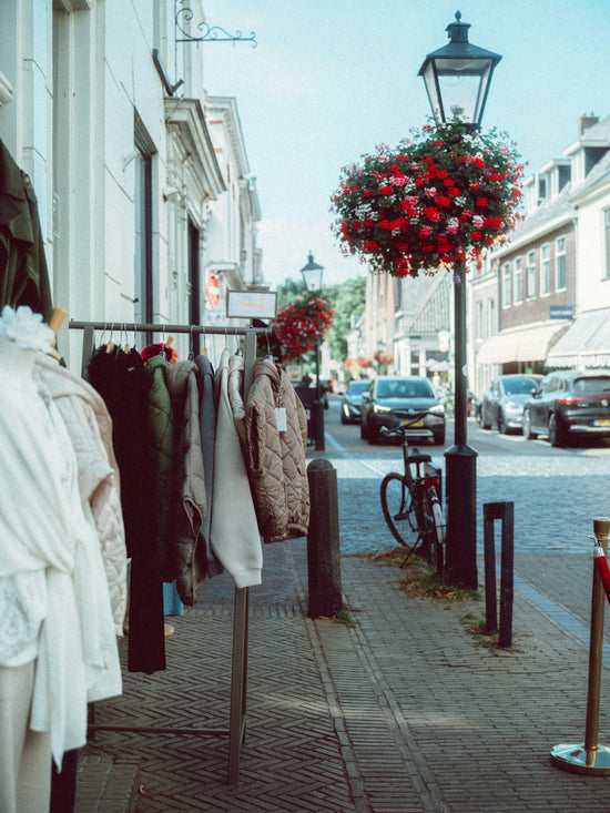 Clothes displayed on racks outside a shop on a street.
