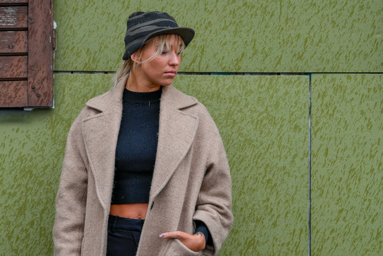 Woman in beige coat and striped hat against green wall.
