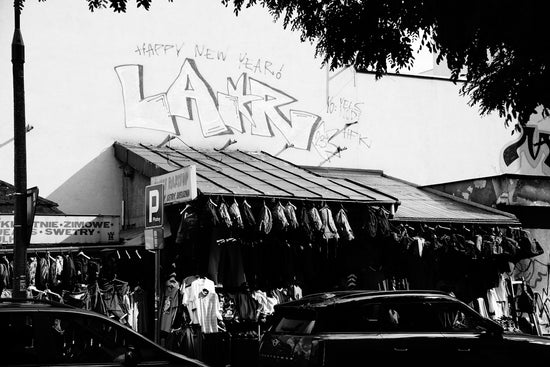 Grayscale urban shopfront with graffiti and clothes on display.